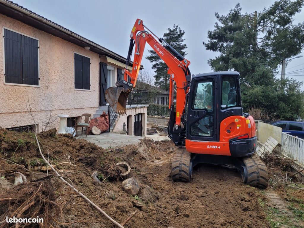 Mini-pelle Kubota U48-4 : Travaux de Terrassement Jardin Mini-pelle orange Kubota U48-4 en plein terrassement d'un jardin devant une maison résidentielle.