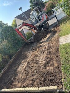 Mini-pelle Neuson en action pour des travaux de terrassement et nivellement de terre dans un jardin résidentiel.
