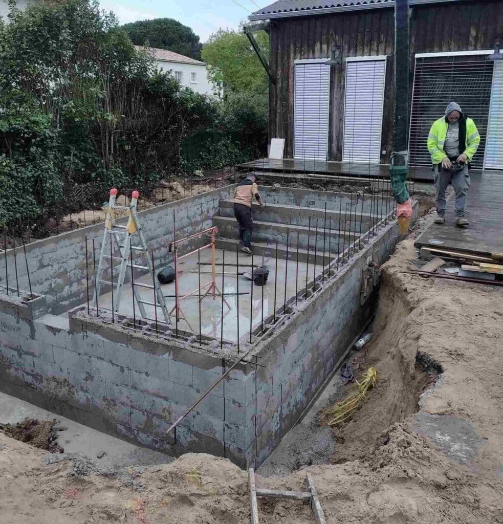 Construction d'une piscine en blocs béton : les étapes Ouvriers sur le chantier de construction d'une piscine en blocs de béton avec fers à béton apparents dans un jardin.