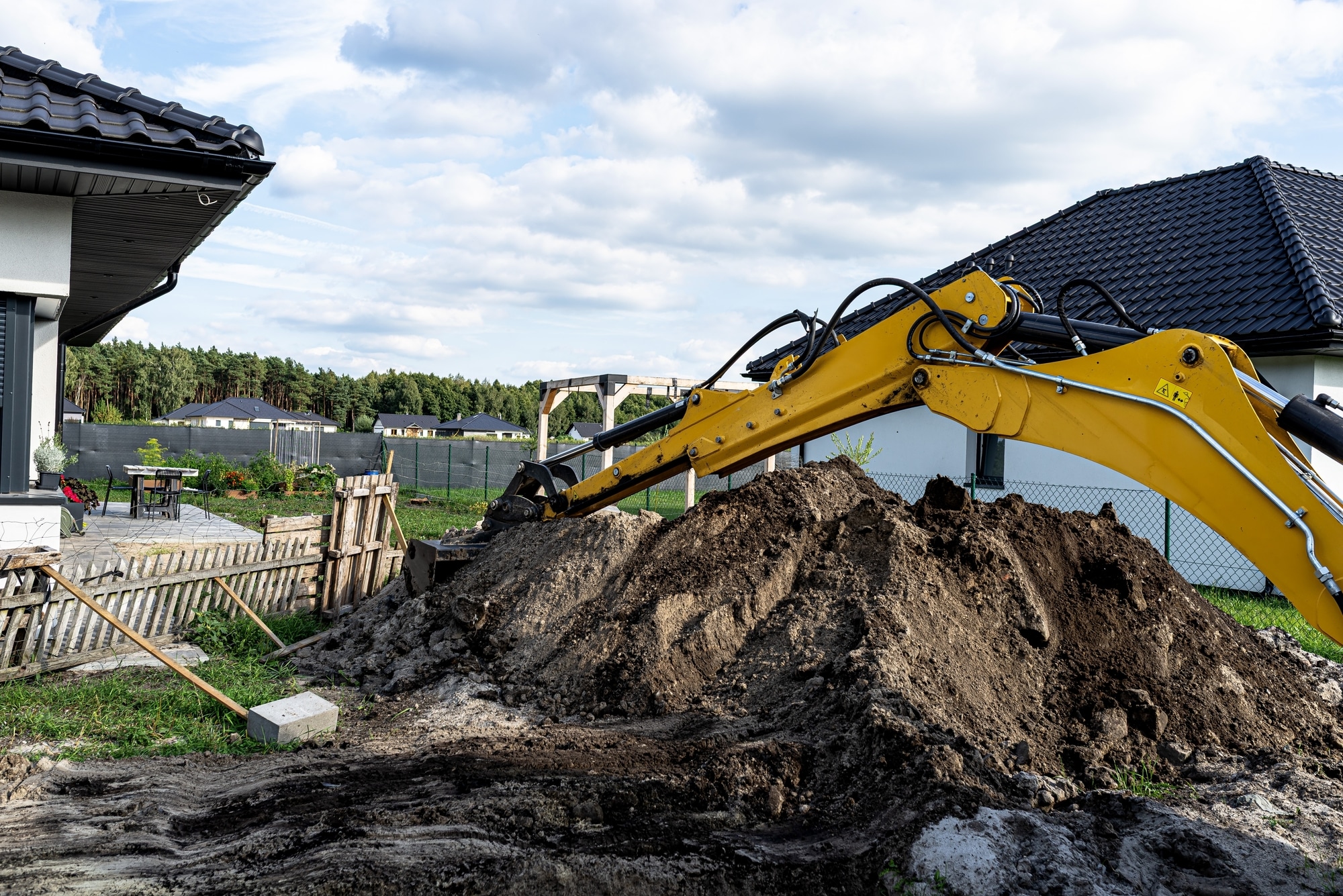 Excavatrice jaune déplaçant de la terre pour des travaux de terrassement dans un jardin résidentiel moderne.